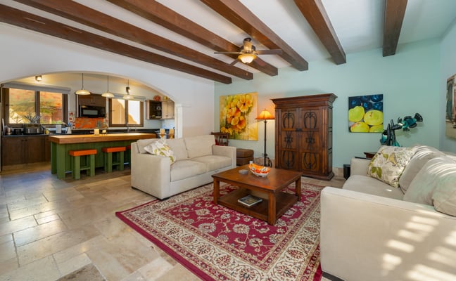 Open-plan living room with exposed wood beams, colourful artwork, and a green kitchen island