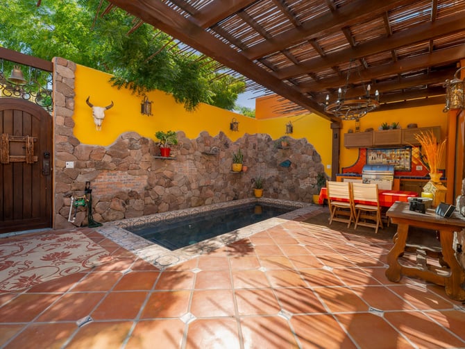 Colourful courtyard with a small pool, stone wall, pergola, and outdoor kitchen