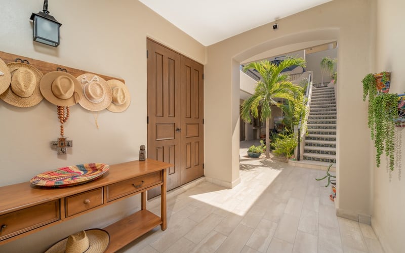Bright entryway with straw hats on a rack, opening to a sunlit courtyard with tiled staircase