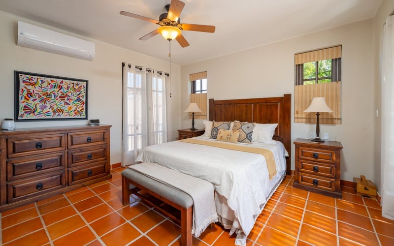 Bedroom with wooden furniture, terracotta tile floor, and colorful Otomi artwork on the wall