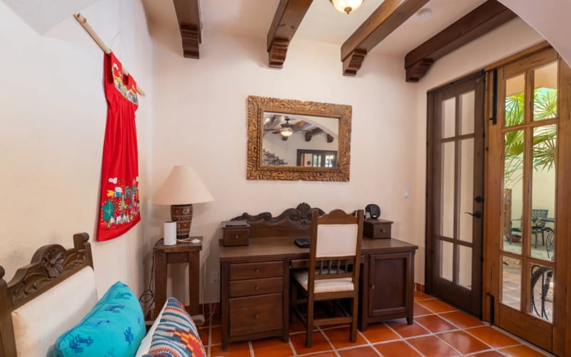 Bedroom nook with carved wooden desk, exposed beam ceiling, and French doors to a garden patio